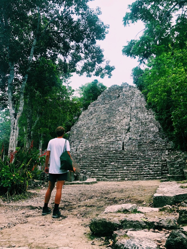Photo of a man looking at a pyramid in the jungle, taken from the back.